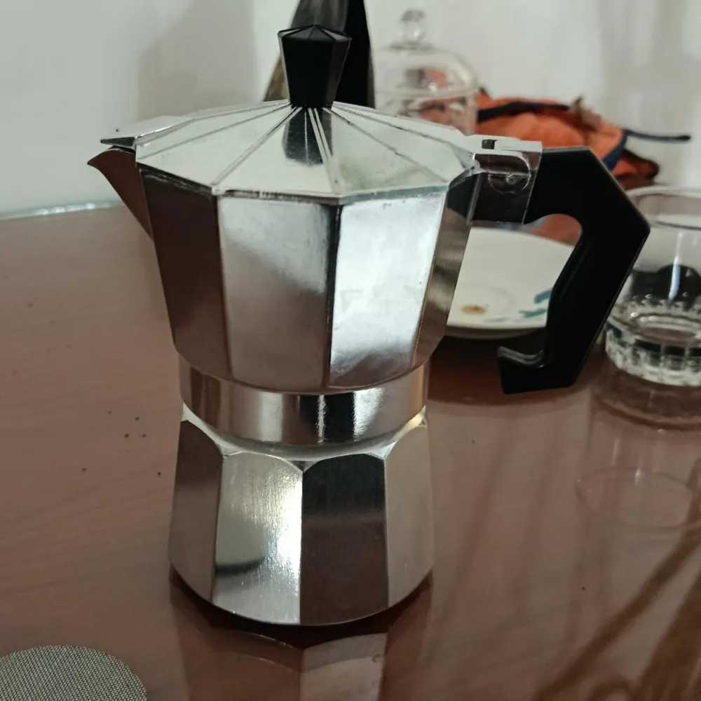 The input: a moka pot on a dining table in dim light with clutter behind it, photographed on a phone